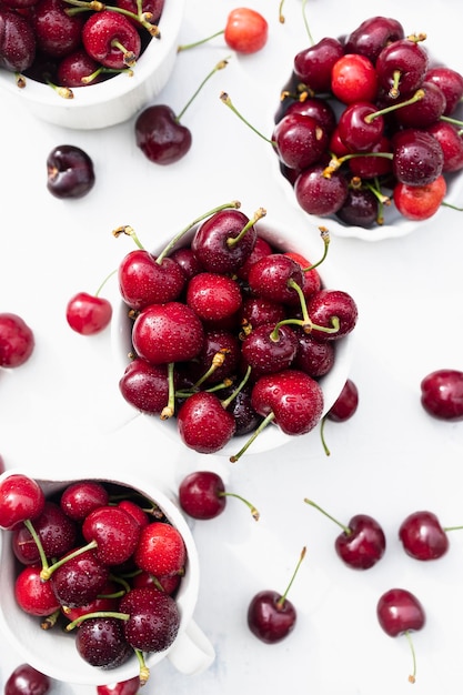 Deliciosas cerezas en tazas de cerámica blanca sobre una mesa de madera blanca