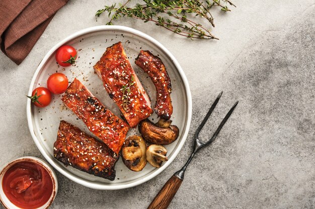 Deliciosas costelas grelhadas temperadas com molho picante e servidas no prato com tomate cereja e cogumelos