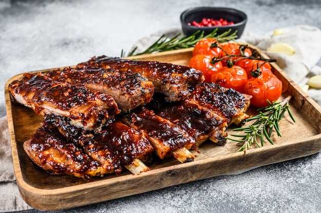 Deliciosas costillas a la parrilla sazonadas con una salsa picante y servidas con tomates al horno. Pared gris. Vista superior