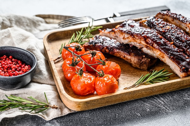 Deliciosas costillas a la parrilla sazonadas con una salsa picante y servidas con tomates horneados. Vista superior