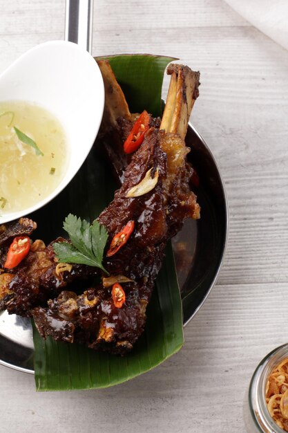 Deliciosas costillas a la parrilla servidas con sopa de caldo en mesa de madera blanca