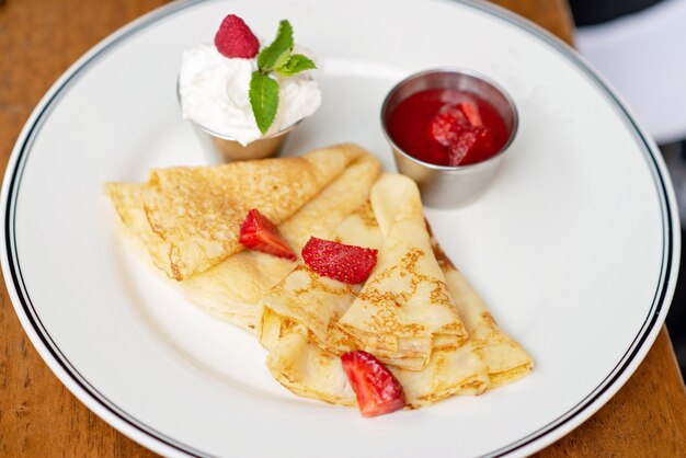 Deliciosas crepas con fresas frescas, hojas de menta y espuma de crema agria. Desayuno en el restaurante. Enfoque selectivo suave.