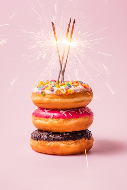 Deliciosas donas para cumpleaños sobre fondo rosa pastel.