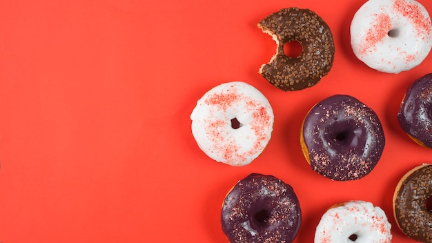 Deliciosas donas con glaseado y mordida faltante sobre fondo rojo