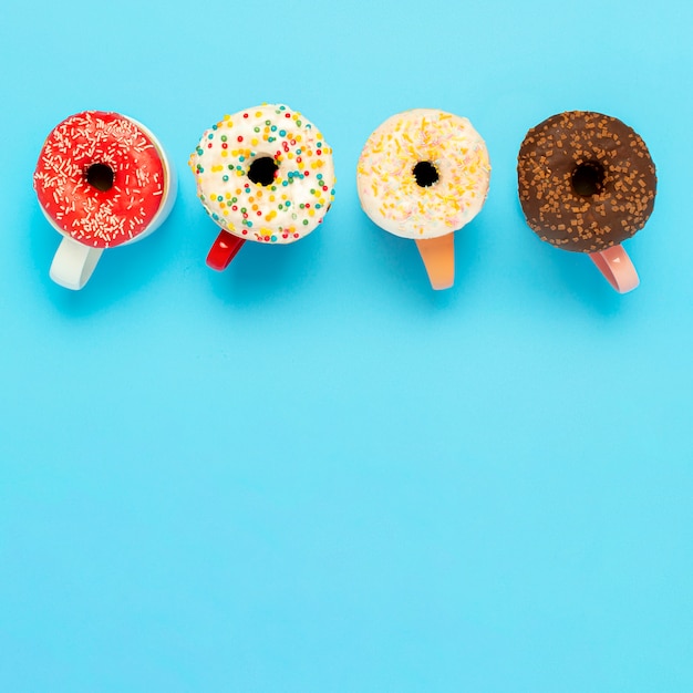 Deliciosas donas y tazas con bebidas calientes en una superficie azul. Concepto de dulces, panadería, pastelería, cafetería. Cuadrado. Vista plana, vista superior