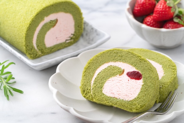 Deliciosas fatias de bolo Matcha Swiss Roll com creme de confeiteiro de morango em fundo branco, close-up.