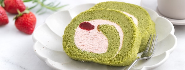 Deliciosas fatias de bolo Matcha Swiss Roll com creme de confeiteiro de morango em fundo branco, close-up.