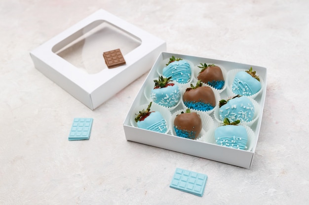 Deliciosas fresas maduras en chocolate marrón y azul en una caja de regalo