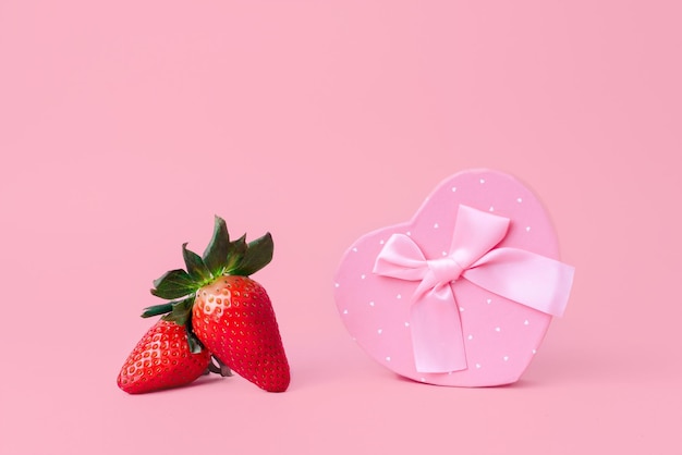 Deliciosas fresas rojas junto a un corazón con una cinta Fondo rosa pastel