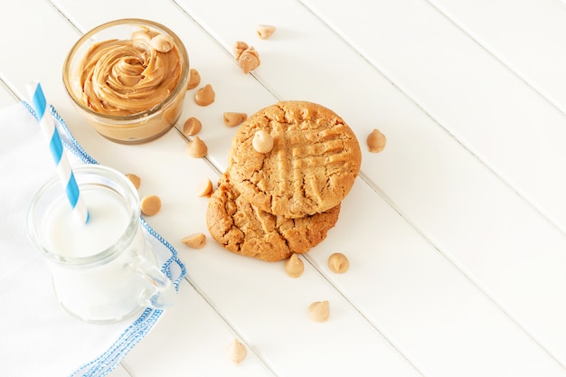 Deliciosas galletas de mantequilla de maní caseras con taza de leche. Espacio de madera blanca. Merienda saludable o sabroso desayuno concepto.