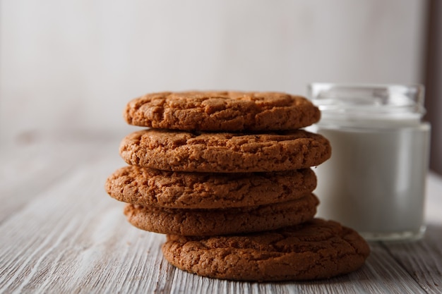 Deliciosas galletas y un vaso de leche en un vaso transparente sobre un fondo blanco rústico.