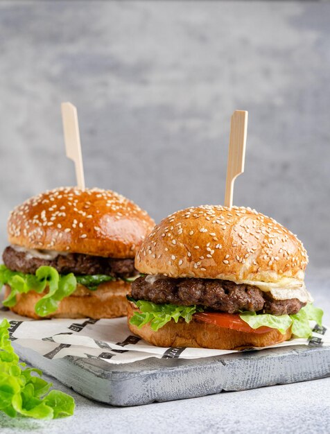 Foto deliciosas hamburguesas caseras con carne salada y verduras frescas en una tabla de cortar gris