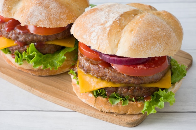 Deliciosas hamburguesas con queso cheddar, tomate, lechuga y cebolla en la mesa de madera blanca