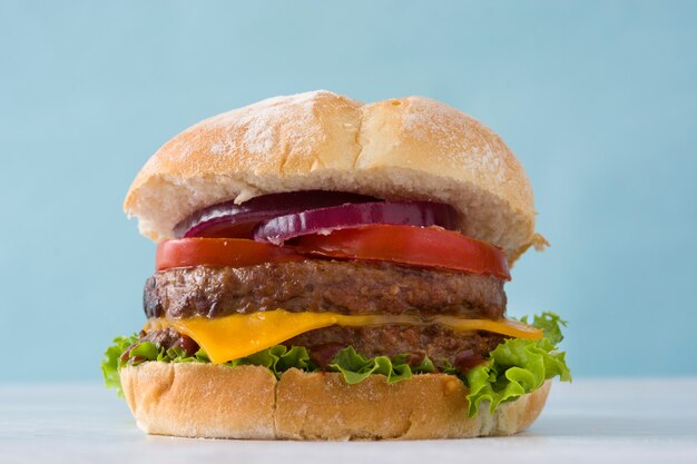 Deliciosas hamburguesas con queso cheddar, tomate, lechuga y cebolla en la mesa de madera blanca