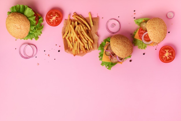 Deliciosas hamburguesas con ternera, tomate, queso, cebolla, pepino y lechuga sobre fondo rosa Vista superior espacio de copia Banner de comida rápida Comida para llevar Concepto de dieta poco saludable