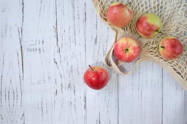Deliciosas maçãs vermelhas maduras em um saco de malha sobre um fundo claro de madeira, vista superior. Nova colheita de verão. O conceito de alimentação saudável.
