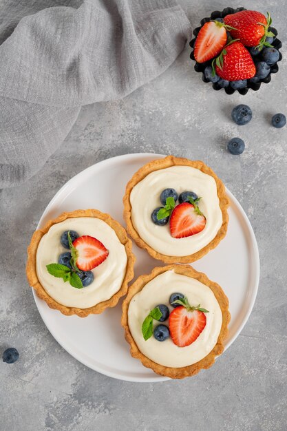 Deliciosas mini tartas con bayas frescas y natillas en una placa blanca.