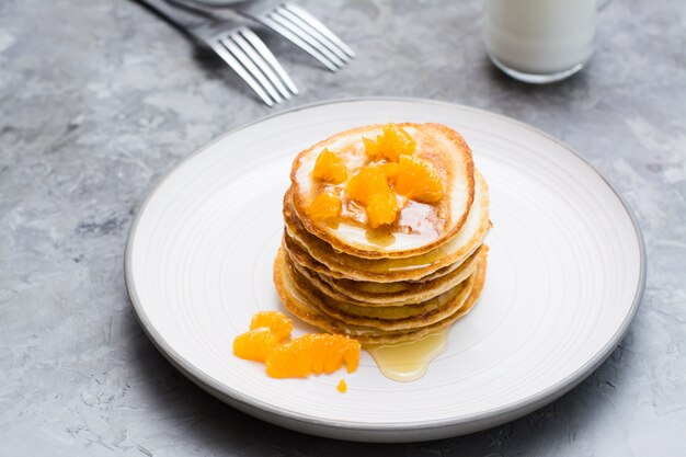 Deliciosas panquecas caseiras com tangerinas e mel, copo de leite em um prato na mesa