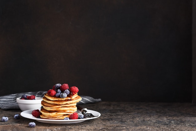 Deliciosas panquecas caseiras em um prato com frutas: framboesas, mirtilos e xarope de bordo.