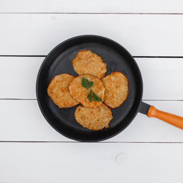 Deliciosas panquecas de batata em uma frigideira sobre uma mesa de madeira branca