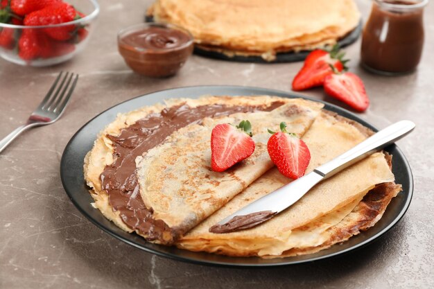 Foto deliciosas panquecas finas com pasta de chocolate e morangos na mesa de mármore cinza