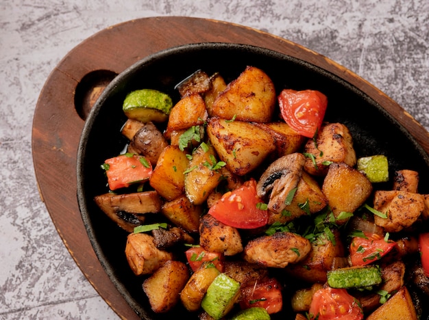 Deliciosas papas al horno con hierbas y verduras en una sartén, estilo rústico. Patatas fritas, tomate cherry rojo, calabacín, cebolla.