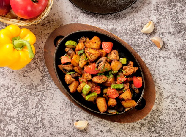 Deliciosas papas al horno con hierbas y verduras en una sartén, estilo rústico. Patatas fritas, tomate cherry rojo, calabacín, cebolla.