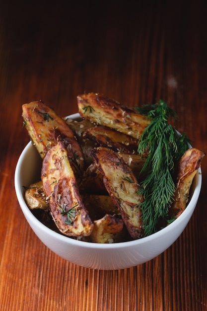 Deliciosas papas al horno en un recipiente de barro con especias, eneldo y cebollas verdes en una mesa de madera, espacio para texto