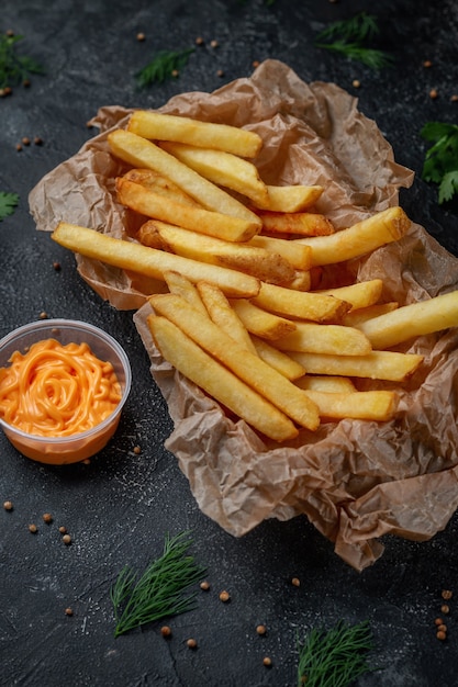 Deliciosas papas fritas crujientes sobre un fondo de piedra oscura con salsa de queso. Restaurante de comida rápida. Opción saludable de comida rápida. Papas fritas