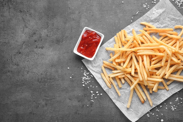 Deliciosas papas fritas y tazón pequeño con salsa sobre fondo gris