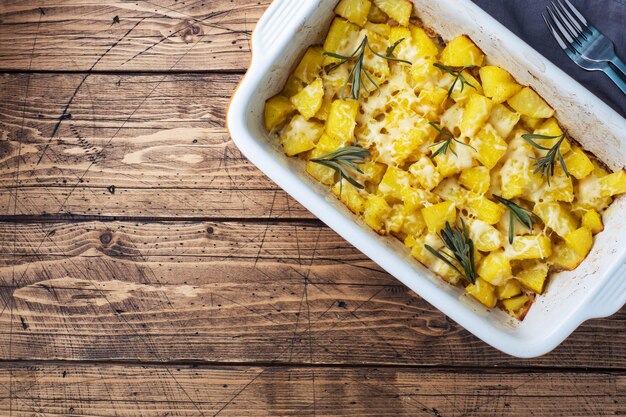 Deliciosas patatas al horno con especias, queso y romero en una bandeja para hornear de cerámica sobre un fondo rústico de madera. Copia espacio