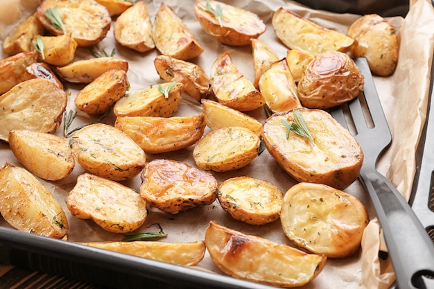 Deliciosas patatas al horno con romero en bandeja para hornear, primer plano