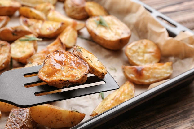 Deliciosas patatas al horno con romero en una espátula encima de la bandeja para hornear, primer plano