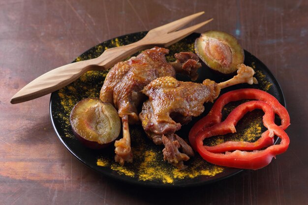 Deliciosas pernas de pato com crosta dourada closeup Duas pernas de pato assado com ameixas de pimentão vermelho e açafrão em uma placa preta em um fundo escuro