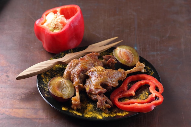 Deliciosas pernas de pato com crosta dourada closeup Duas pernas de pato assado com ameixas de pimentão vermelho e açafrão em uma placa preta em um fundo escuro