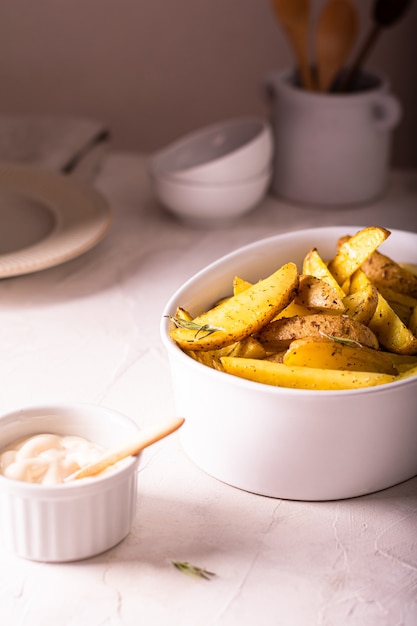 Deliciosas rodajas de patatas al horno con romero y aceite en un recipiente de cerámica