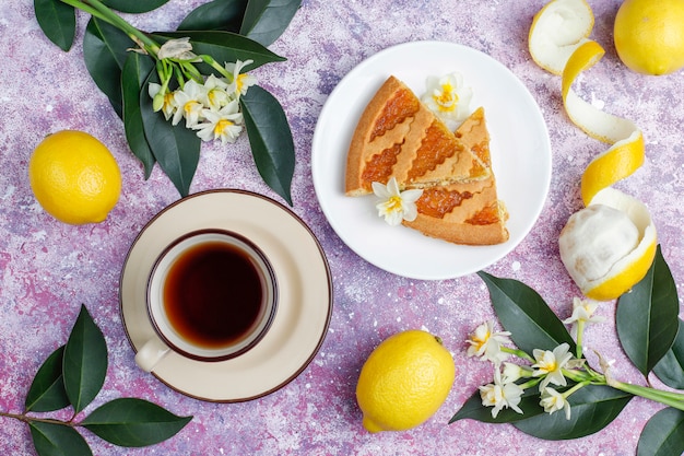 Deliciosas rodajas de tarta de limón con limones frescos y una taza de té en concreto, vista superior