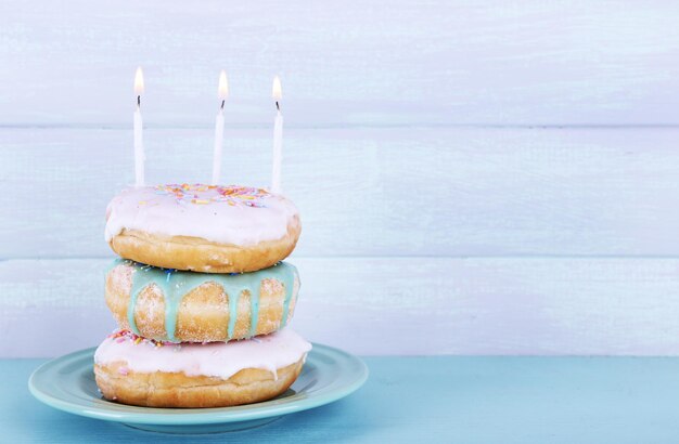 Foto deliciosas rosquillas con glaseado y velas de cumpleaños en la mesa sobre fondo de madera