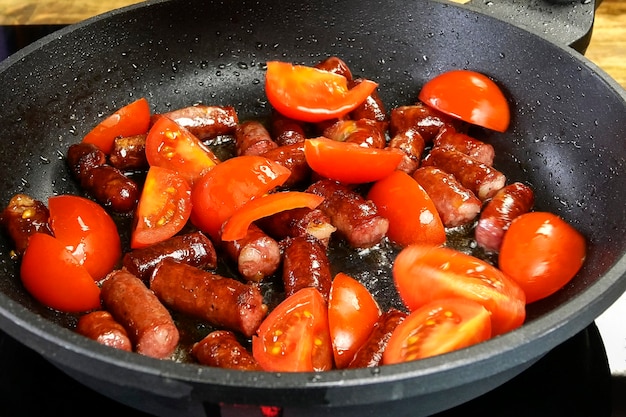 Deliciosas salsichas gordurosas de caça cortadas em pedaços e fatias de tomate são fritas na frigideira