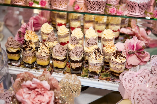 Deliciosas sobremesas na barra de chocolate do casamento na área do buffet: copos com sobremesa em camadas com chocolate, natas, nozes, suflê, chantilly