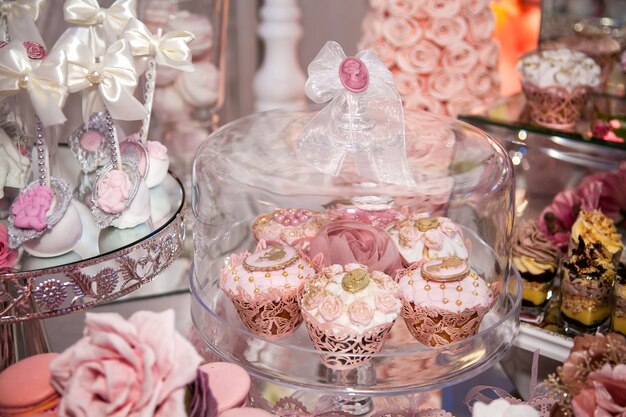 Deliciosas sobremesas na barra de chocolate do casamento na área do buffet: muffins decorados com anjos, camafeu, botões de rosa açucarados e corante dourado.