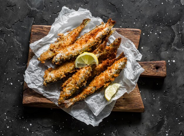 Deliciosas tapas aperitivo sardinas fritas en migas de pan en una tabla de cortar en una vista superior de fondo oscuro