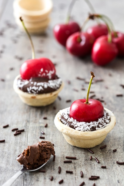 Deliciosas tartaletas de chocolate con cereza roja y coco en una rústica mesa de madera