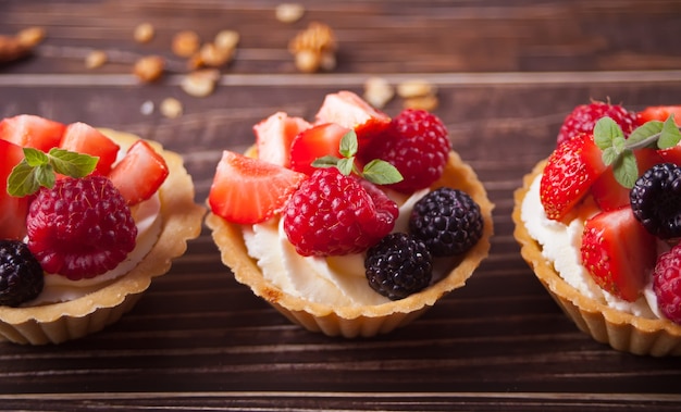 Deliciosas tartaletas mini tarta con bayas frescas en mesa de madera.