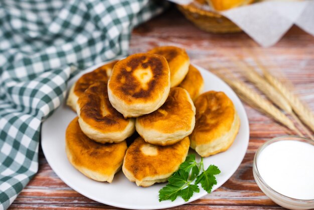 Deliciosas tartes fritas caseiras com batatas e carne com creme azedo na mesa de madeira da cozinha Closeup