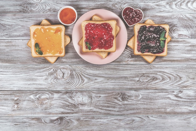 Deliciosas tostadas con diversas mermeladas dulces sobre fondo gris. Copyspace para su texto, banner.