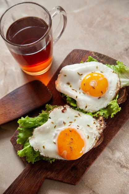 Deliciosas tostadas con huevos fritos y hojas de lechuga para el desayuno colocados en la mesa cerca de una taza de té caliente en la mañana