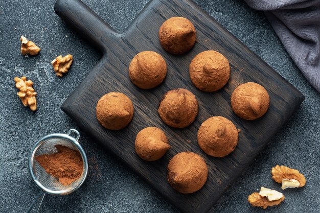 Deliciosas trufas de chocolate espolvoreadas con cacao en polvo y nueces sobre un soporte de madera. Fondo de hormigón oscuro