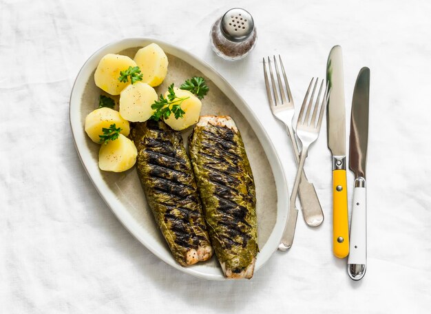 Delicioso almuerzo tapas aperitivo caballa a la parrilla envuelto en hojas de uva y patatas hervidas en una vista superior de fondo claro