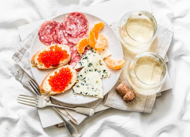 Delicioso aperitivo sándwiches de caviar rojo queso azul salami mandarinas y vino blanco